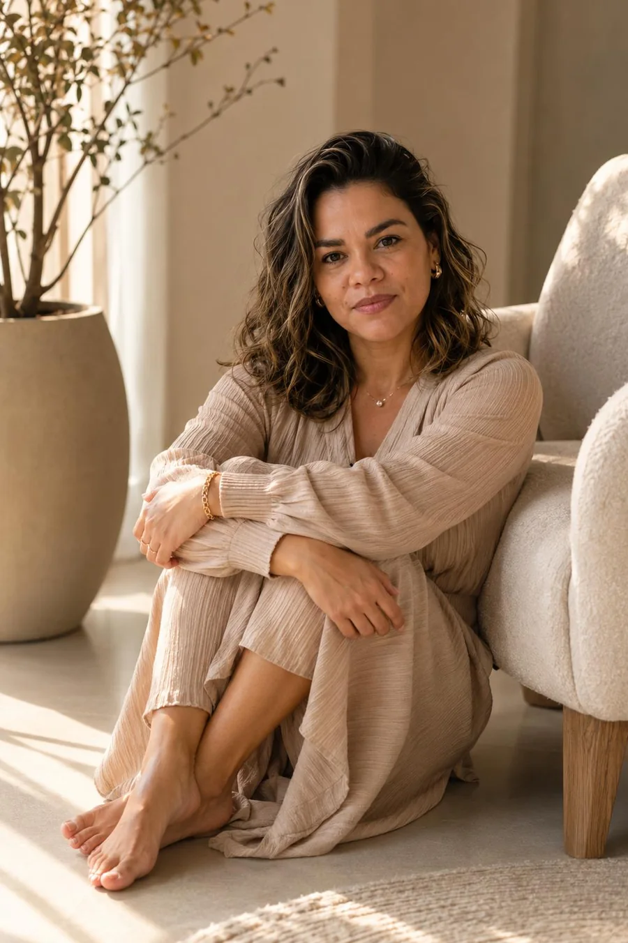 Milca Katherine sentada no chão de uma sala clara, ao lado de uma poltrona